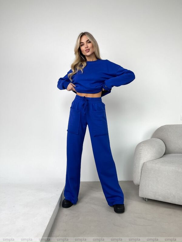 Woman wearing a blue outfit standing in a minimalistic room with a gray sofa.