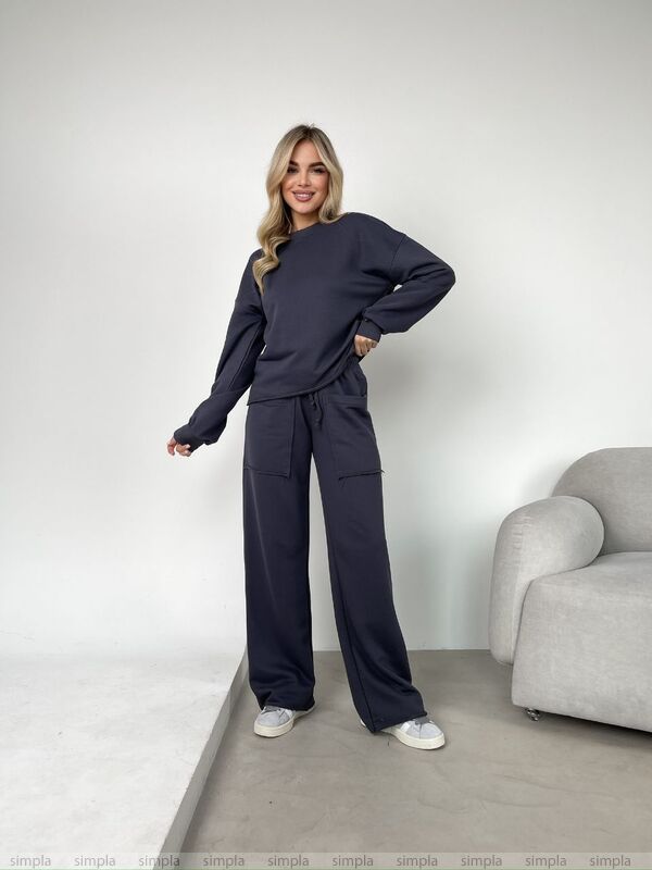 Woman wearing a navy tracksuit standing in a minimalistic room with a gray armchair.