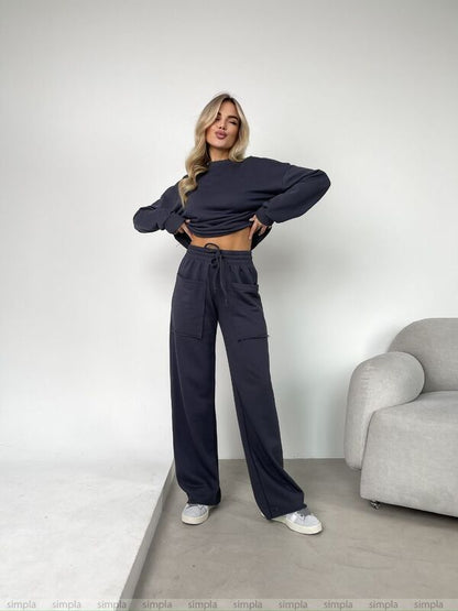 Woman wearing a dark blue outfit standing in a minimalistic room with a gray chair.