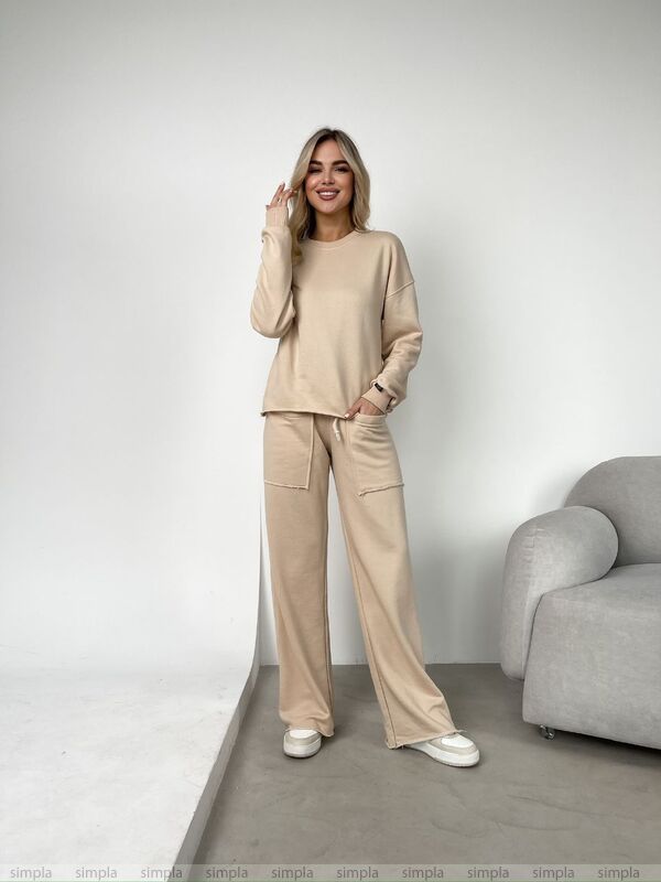 Woman wearing a beige outfit standing in a minimalistic room with a gray armchair.