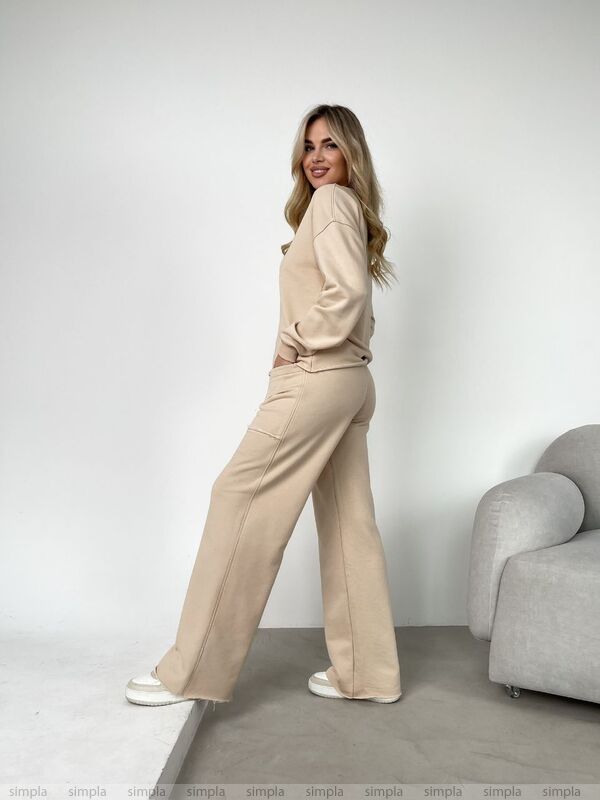 Woman in a beige outfit standing in a minimalistic room with a gray sofa.