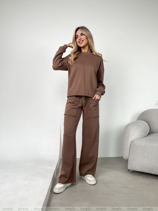 Woman wearing a brown outfit standing in a minimalistic room with a gray chair.