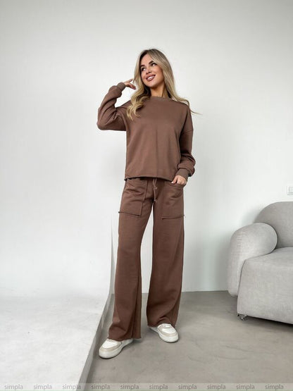 Woman wearing a brown outfit standing in a minimalistic room with a gray chair.