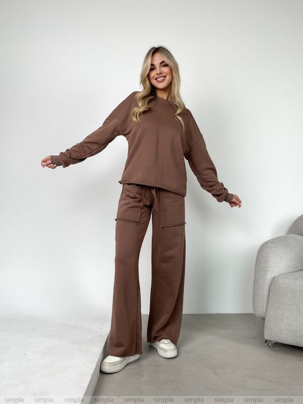 Woman wearing a brown outfit standing in a minimalistic room with a gray chair.