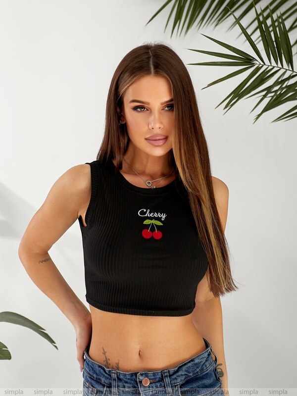 Woman wearing a black tank top with 'Cherry' design, standing against a light background with green leaves.