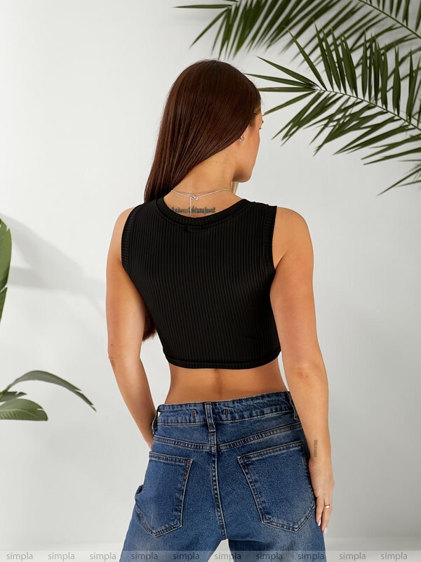 Person wearing a black ribbed tank top and blue jeans against a white background with green leaves.