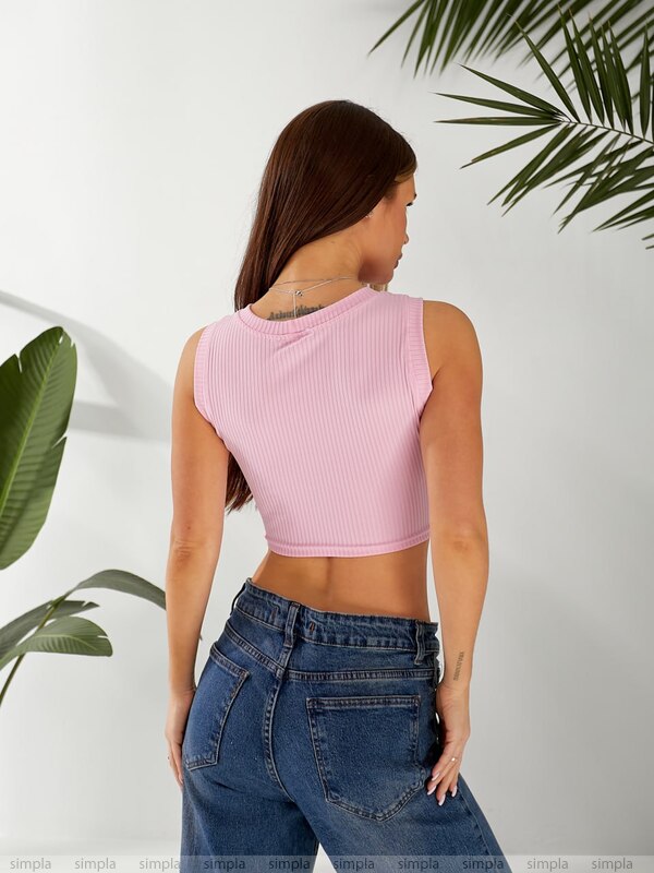 Woman wearing a pink crop top and blue jeans with green leaves in the background