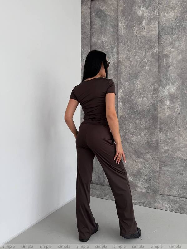 Woman wearing a brown outfit against a gray wall.