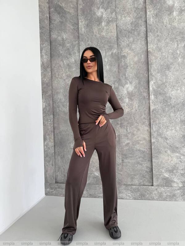 Woman wearing a brown outfit standing against a gray textured wall.