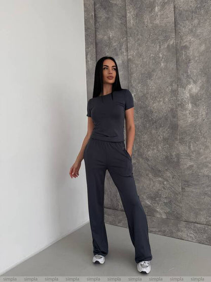 Woman wearing a dark gray outfit standing against a textured wall.