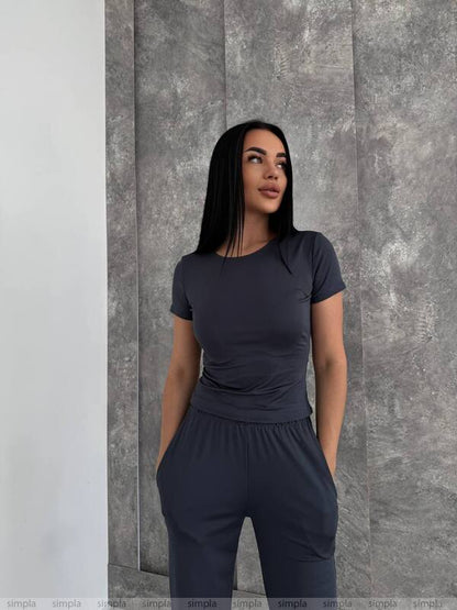 Woman wearing a dark gray outfit against a textured wall.