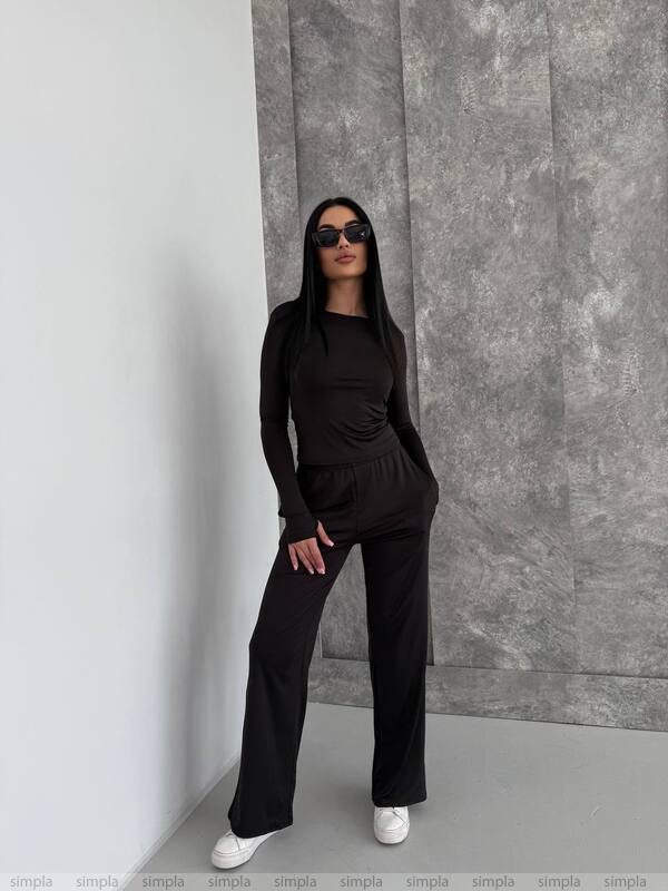 Person wearing a black outfit against a gray wall