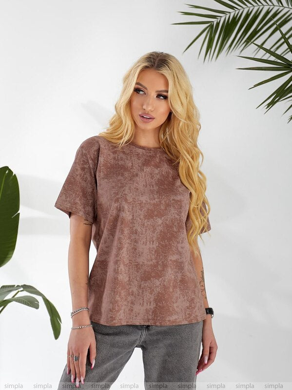 Woman wearing a brown t-shirt and gray pants against a white background with green leaves.