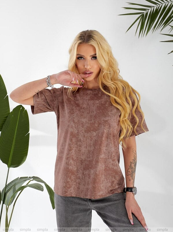 Woman wearing a brown t-shirt and gray pants with plants in the background