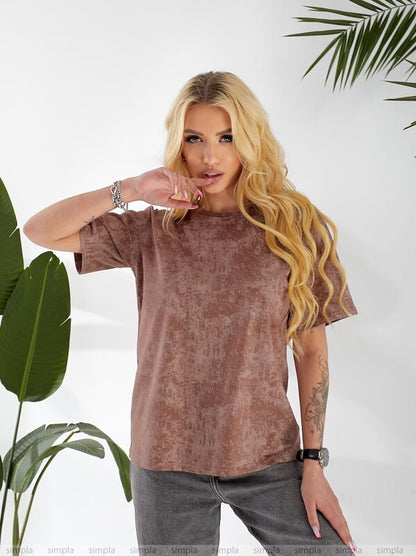 Woman wearing a brown t-shirt and gray pants with plants in the background
