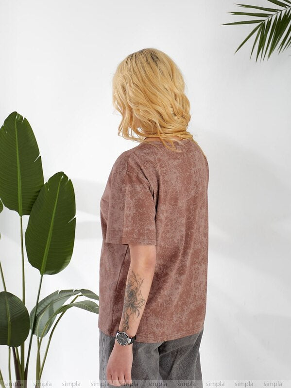 Person wearing a brown t-shirt standing next to a plant against a white background