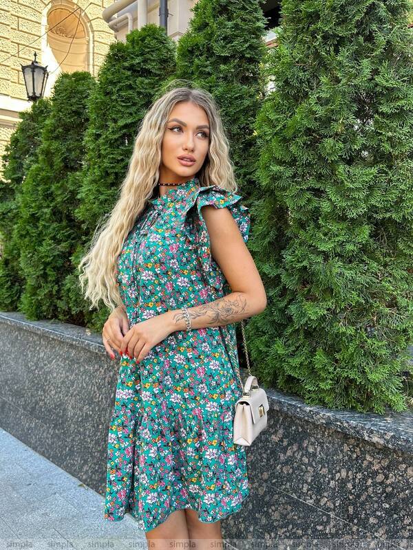 Woman in a floral dress standing outdoors with greenery in the background