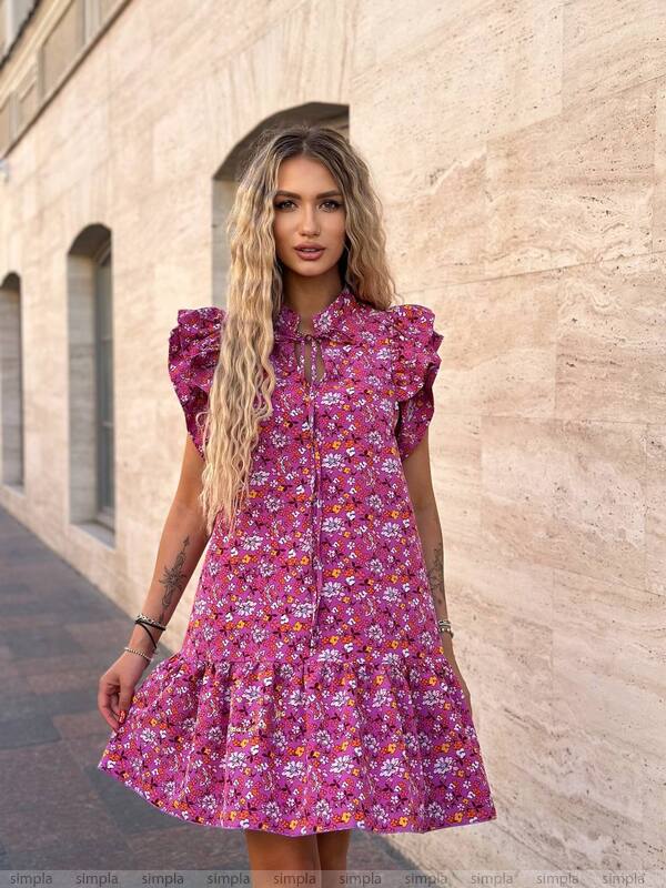 Woman wearing a pink floral dress standing against a beige wall.