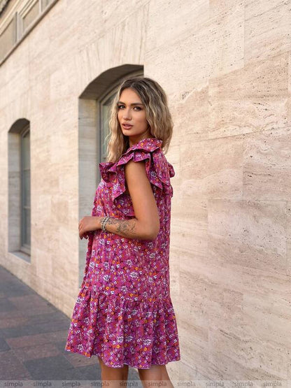 Woman wearing a pink floral dress standing against a beige stone wall.