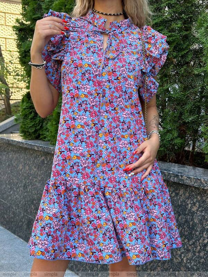 Woman wearing a colorful floral dress standing outdoors with greenery in the background