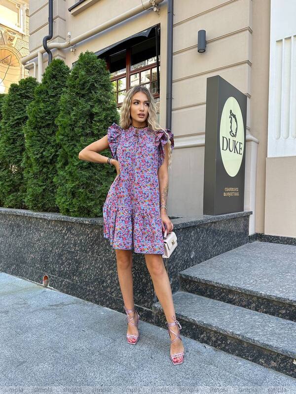 Woman in a floral dress standing outside a building with a 'Duke' sign.
