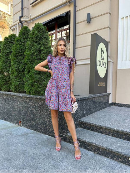 Woman in a floral dress standing outside a building with a 'Duke' sign.