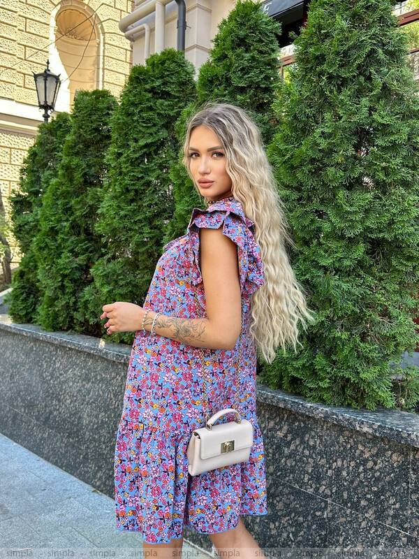 Woman in a floral dress standing outdoors with greenery in the background