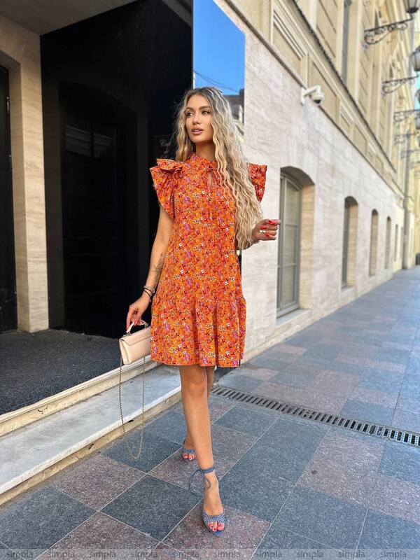Woman in an orange floral dress standing on a city street.