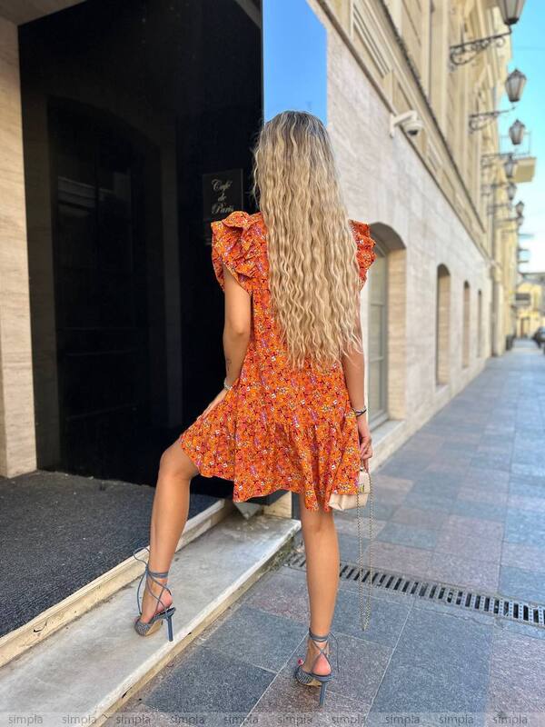 Woman in an orange dress standing on a street with buildings in the background