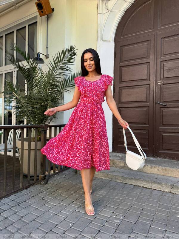 Woman in a pink dress standing on a sidewalk with a white bag.
