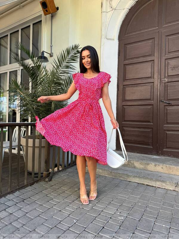 Woman in a pink dress standing on a sidewalk with a building in the background