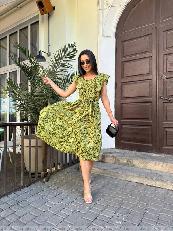 Woman in a green dress posing outdoors near a building entrance.