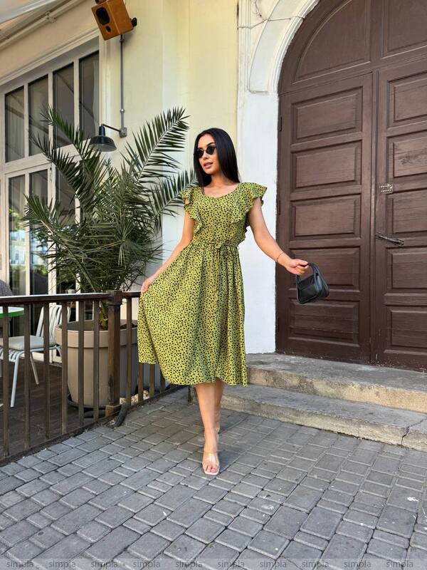 Woman in a green dress walking outside a building with a plant and door in the background.
