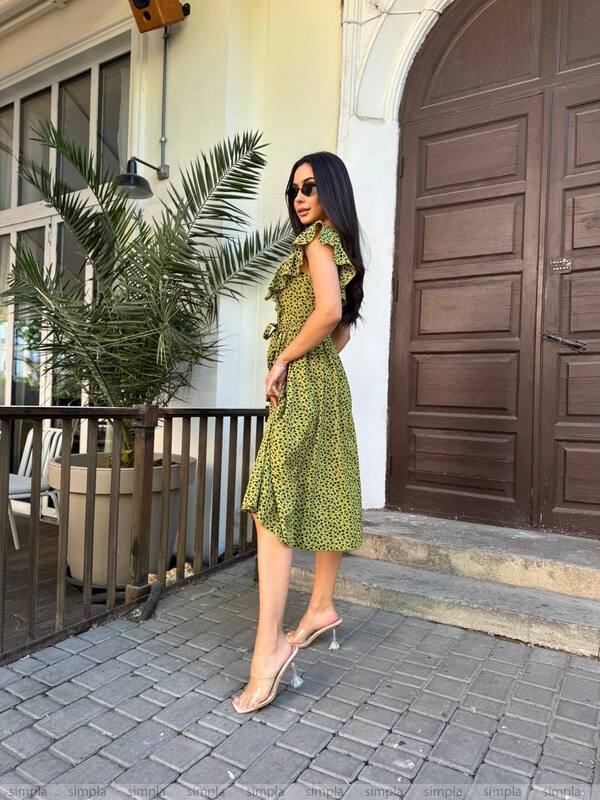 Woman in a green dress standing on a sidewalk with a building in the background