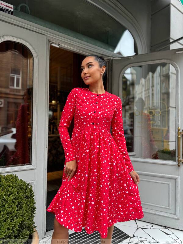 Woman in a red dress with white polka dots standing outside a building.