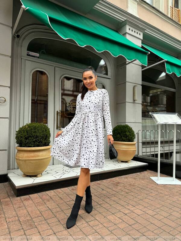Woman in a white dress with black patterns standing in front of a store with a green awning.