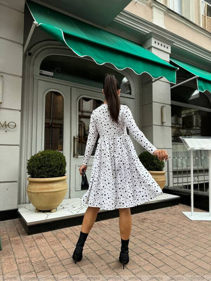 Woman in a polka dot dress walking past a building with a green awning.