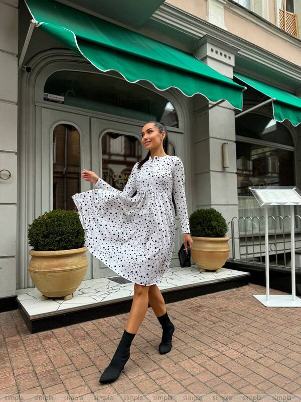 Woman in a white polka dot dress standing in front of a store with a green awning.