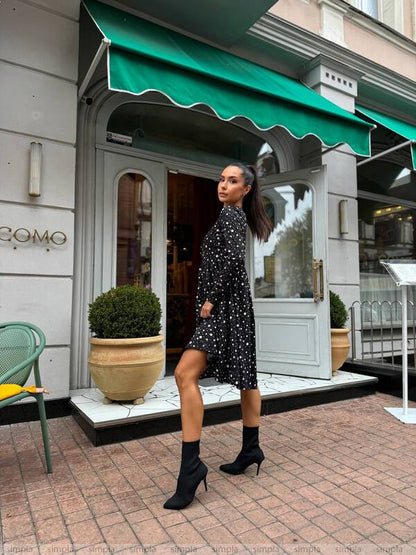 Woman in a black polka dot dress standing in front of a building with a green awning.