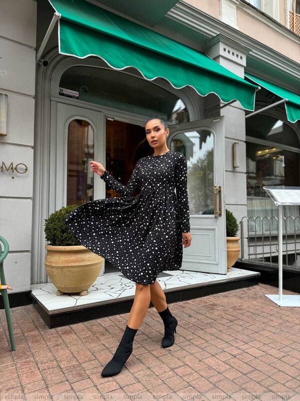 Woman in a black polka dot dress standing in front of a store with a green awning.