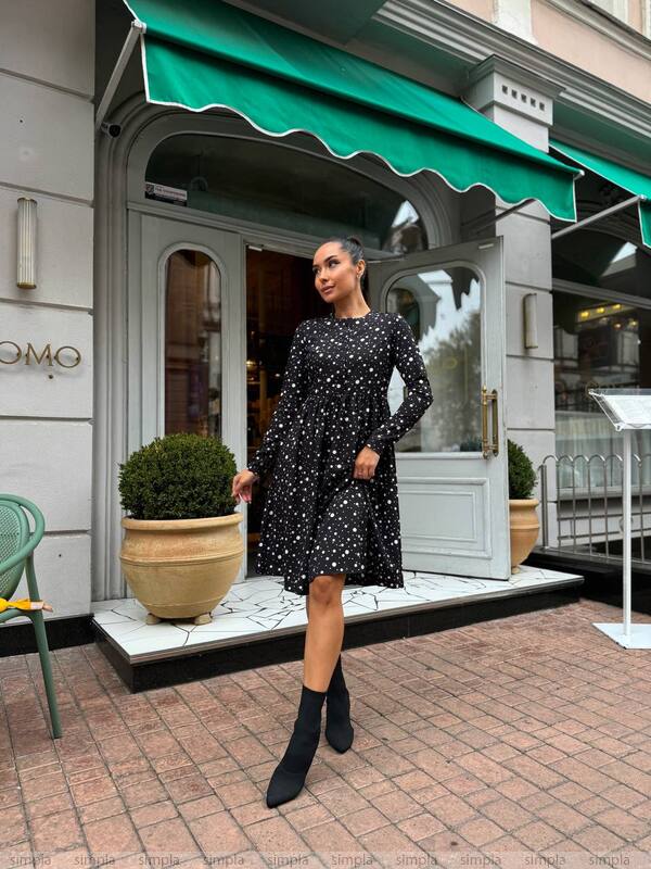 Woman in a black polka dot dress standing in front of a store with a green awning.