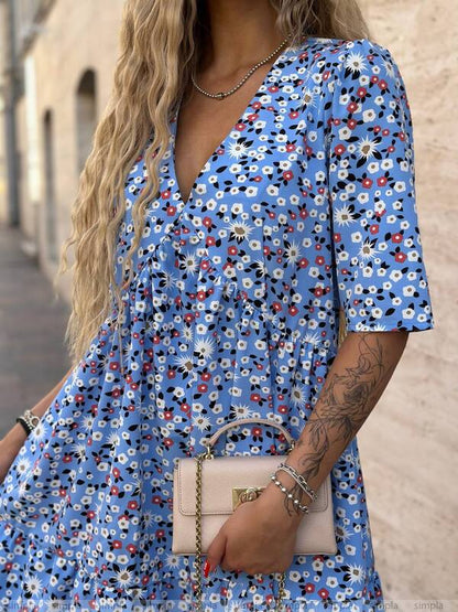 Woman wearing a blue floral dress holding a beige handbag.