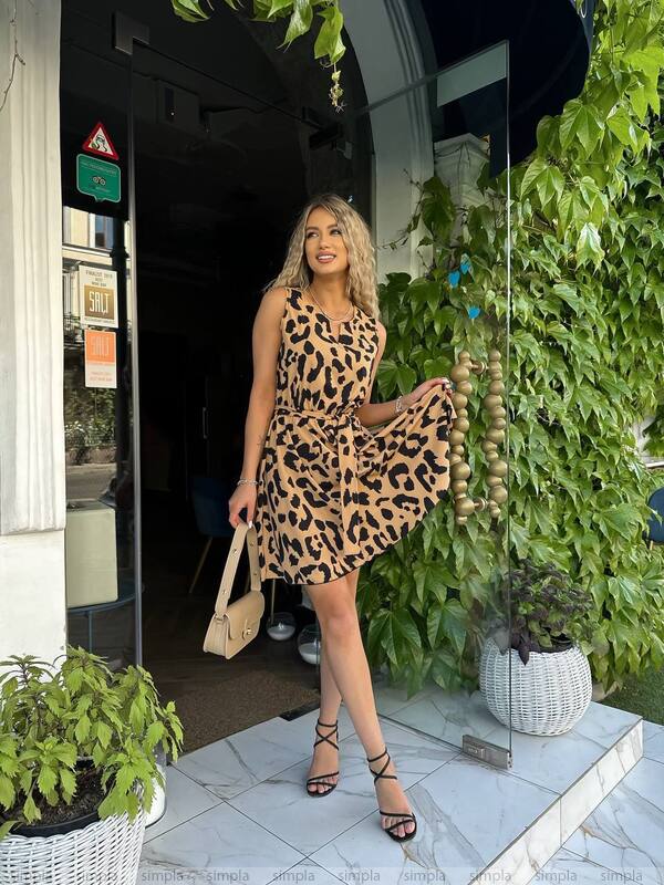 Woman in a leopard print dress standing outside a building with plants around.