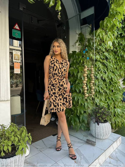 Woman in a leopard print dress standing outside a building with greenery.