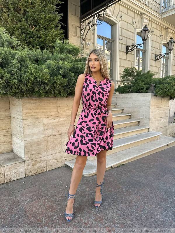 Woman in a pink leopard print dress standing in front of a building entrance.