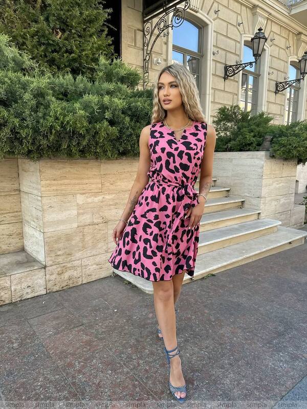 Woman wearing a pink dress with black leopard print standing outdoors.