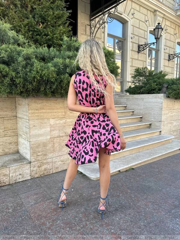 Woman in a pink leopard print dress standing on a street with a building in the background