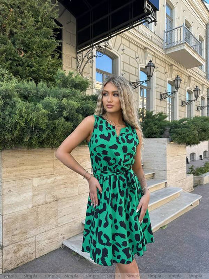 Woman in a green dress with black patterns standing in front of a building.