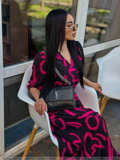 Woman in a black and pink dress with a YSL bag sitting on a chair.