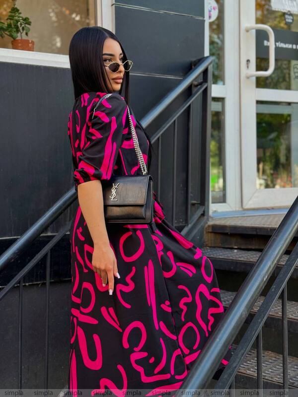 Woman in a black and pink patterned dress with a YSL bag on a city street.